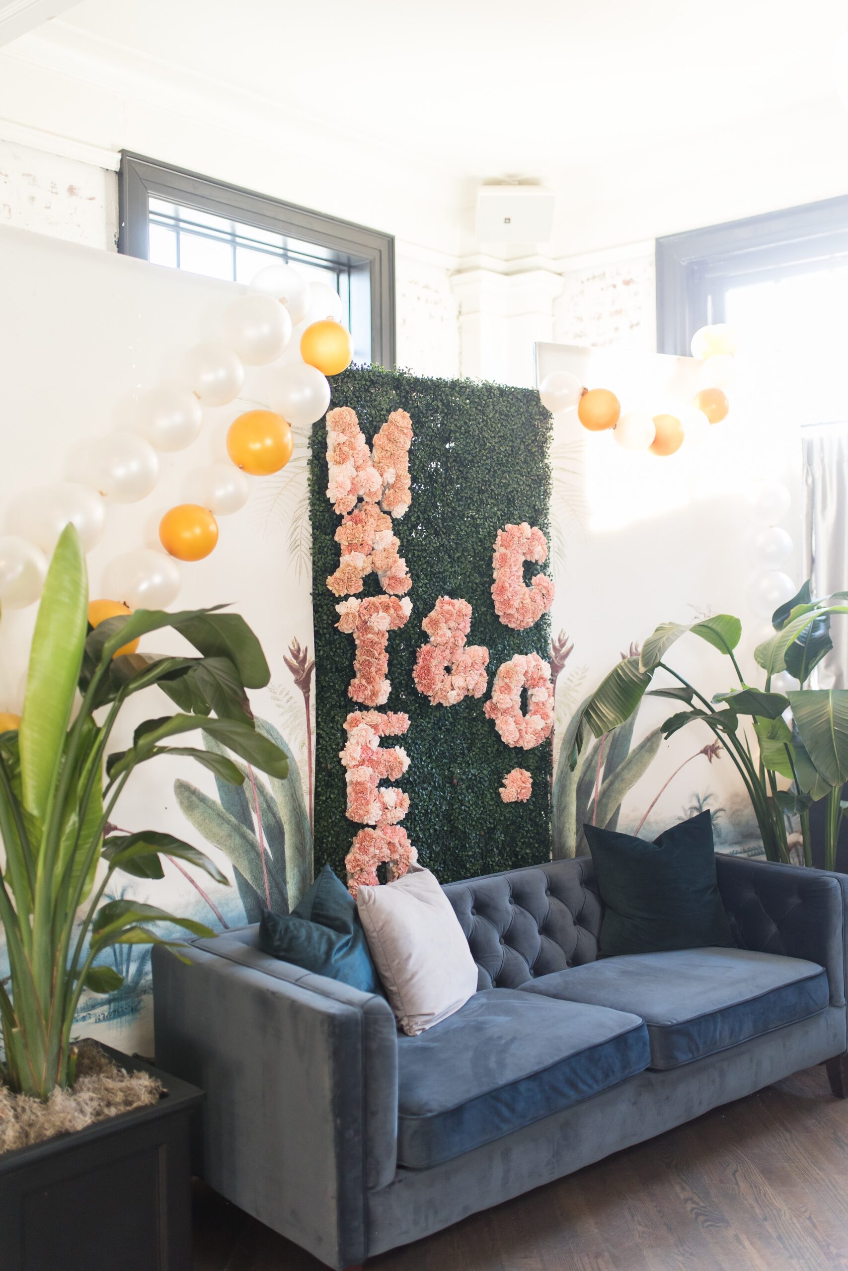 Custom floral wall for photos with a blue velvet couch in front.