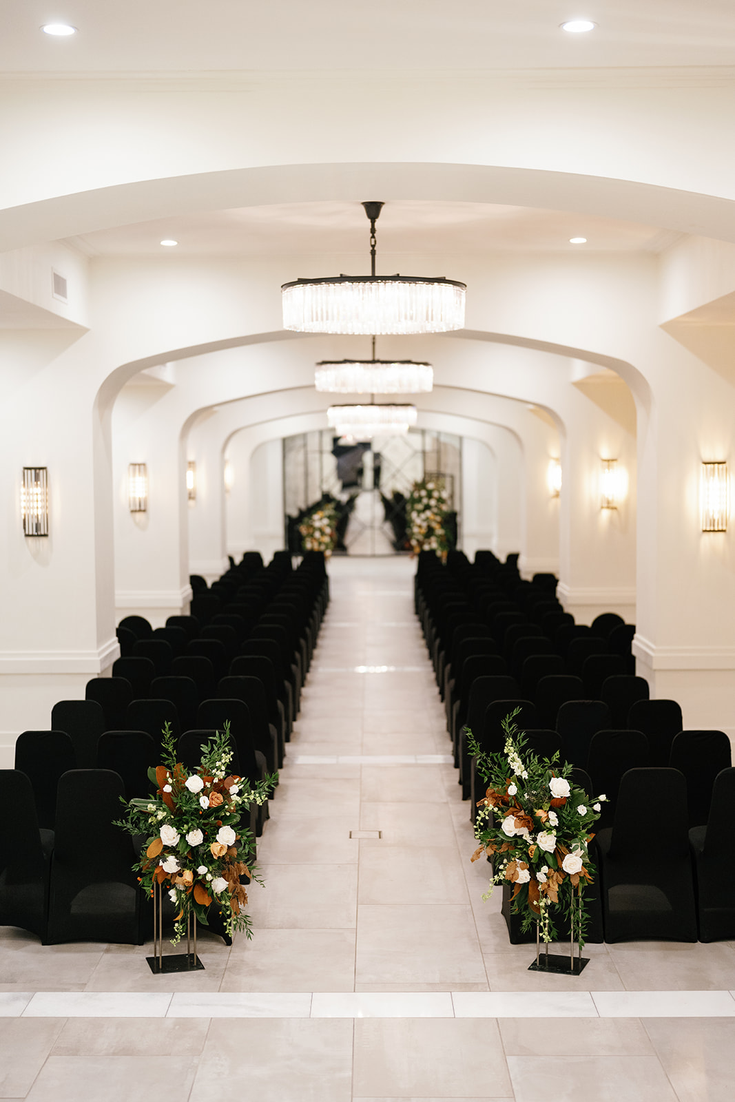 A wedding ceremony site with beautiful chandeliers and black chairs.