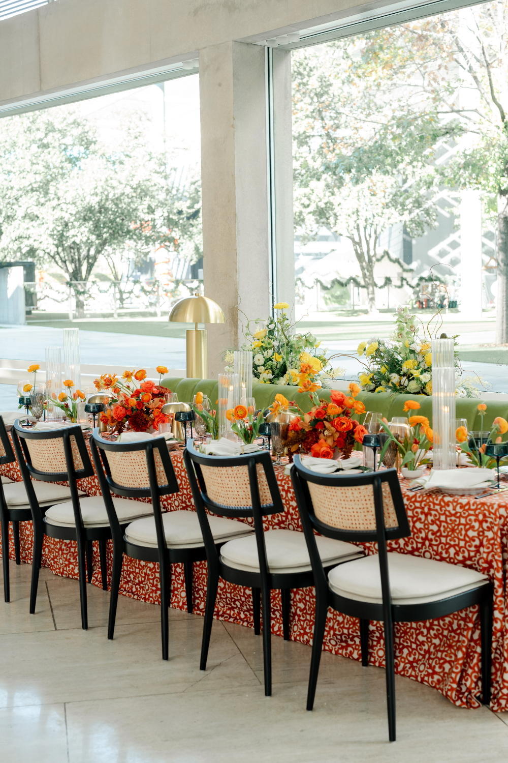 Black and rattan chairs pulled up to an orange printed linen table with bright orange and yellow florals and gold lamps.