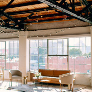 A custom lounge area for a wedding reception with a leather couch, two barrel chairs, a rug, and small tables.