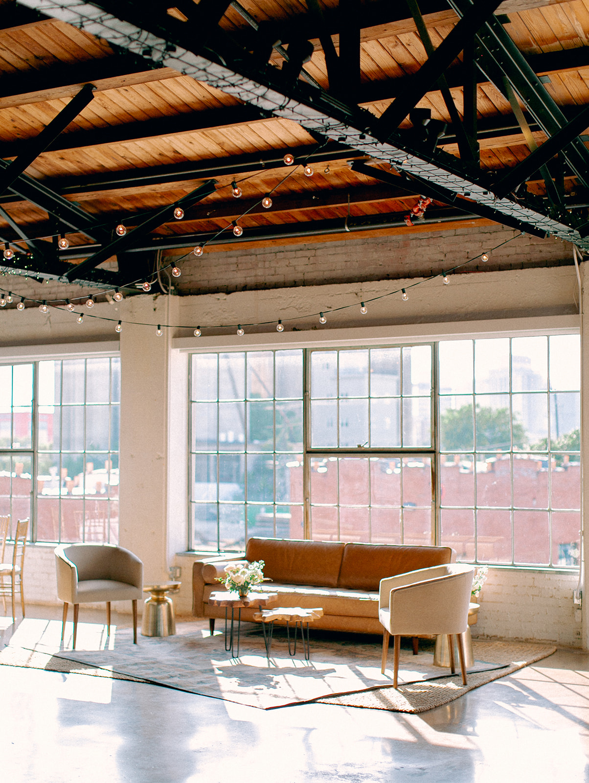 A custom lounge area for a wedding reception with a leather couch, two barrel chairs, a rug, and small tables.